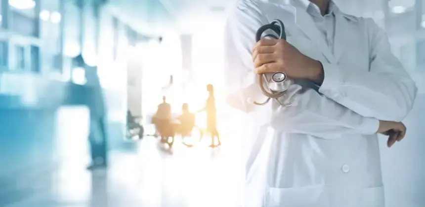 Médico con bata blanca sosteniendo un estetoscopio en un pasillo de hospital iluminado