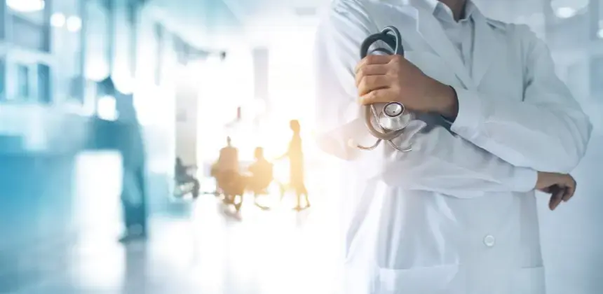 Médico de bata blanca sosteniendo un estetoscopio en un pasillo hospitalario iluminado