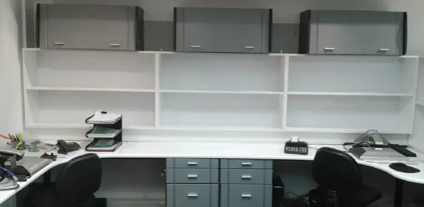 Escritorio de oficina con estanterías y gabinetes grises, sillas giratorias y accesorios de trabajo organizados