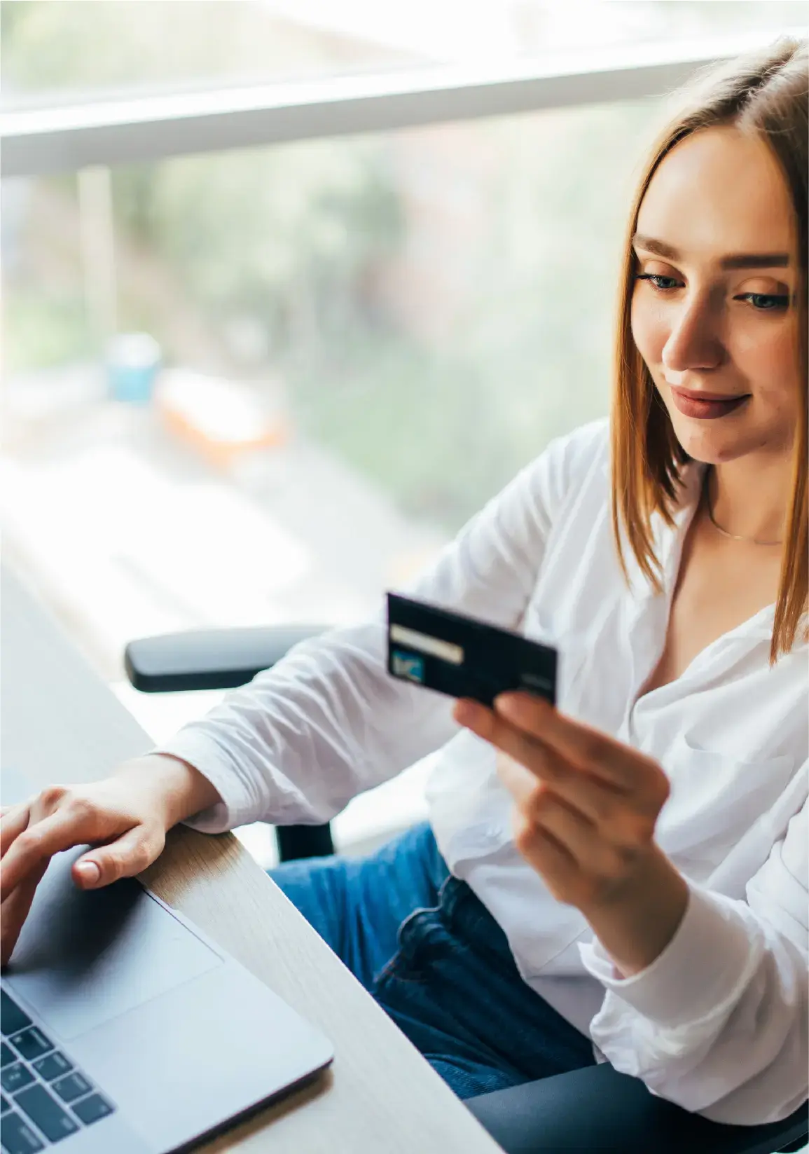 Mujer joven usando su tarjeta de crédito para hacer una compra en línea desde una computadora portátil.