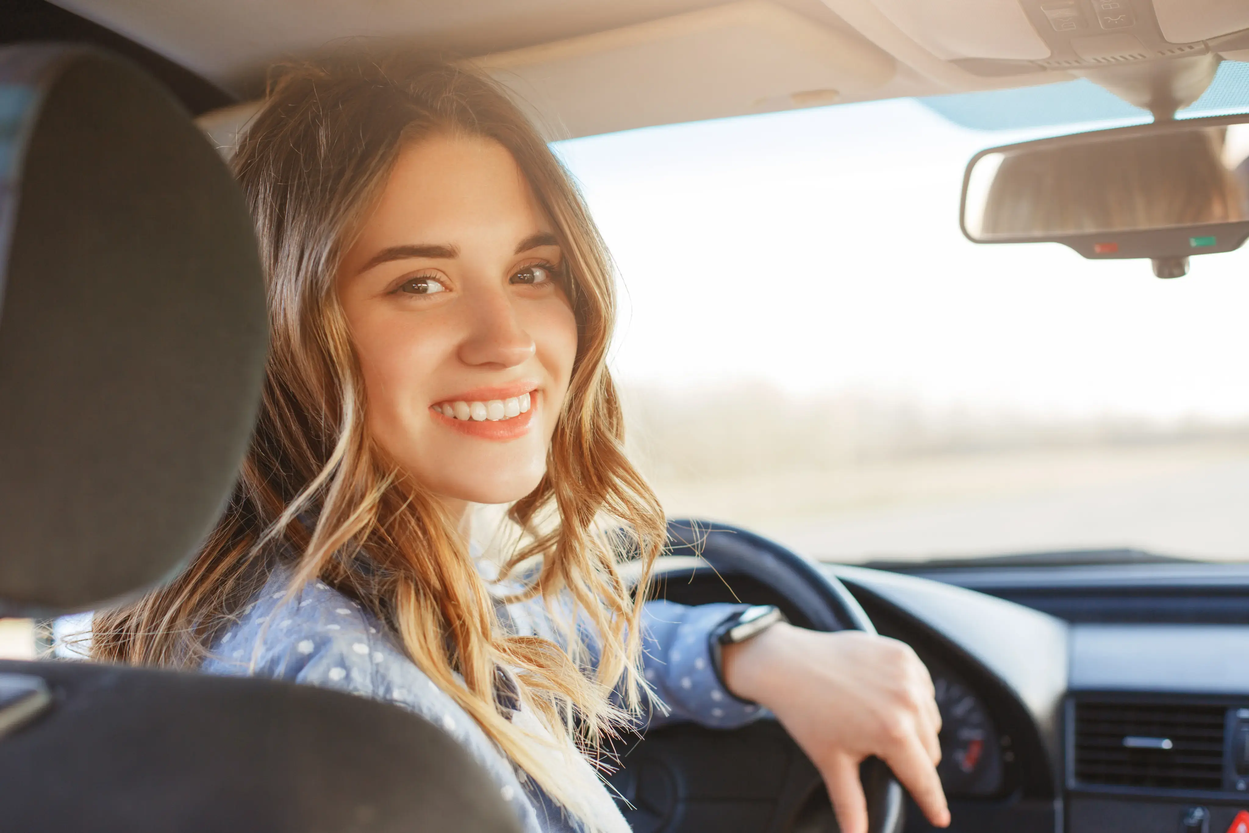 Mujer sonriendo mientras conduce un automóvil y mira hacia la cámara.