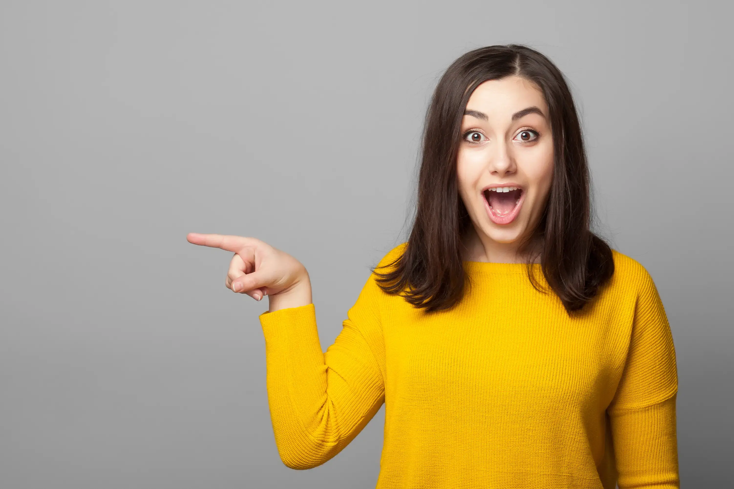 Mujer con suéter amarillo señalando hacia un lado con expresión de sorpresa.