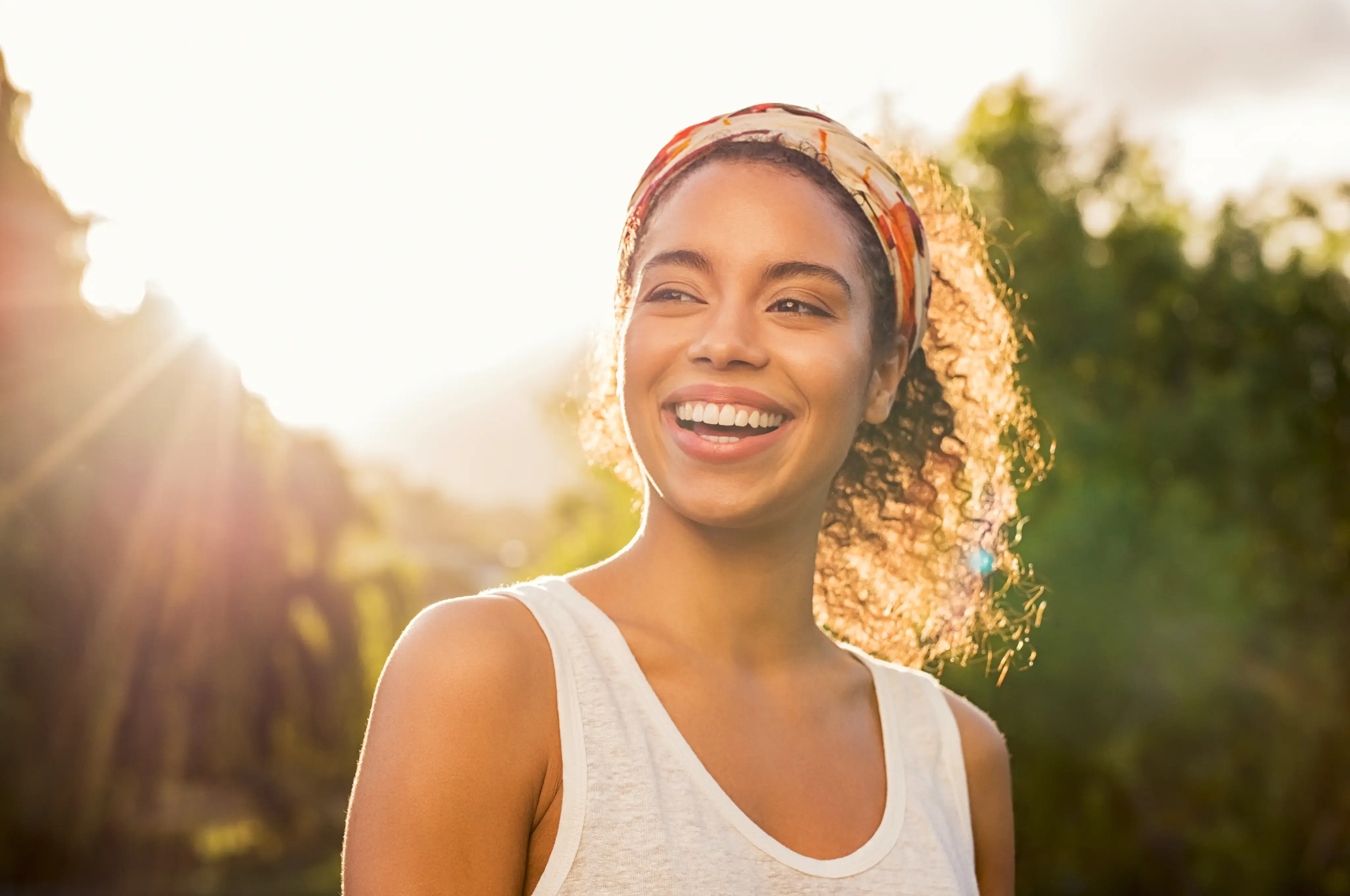 Mujer sonriendo al aire libre con luz de sol detrás de ella.