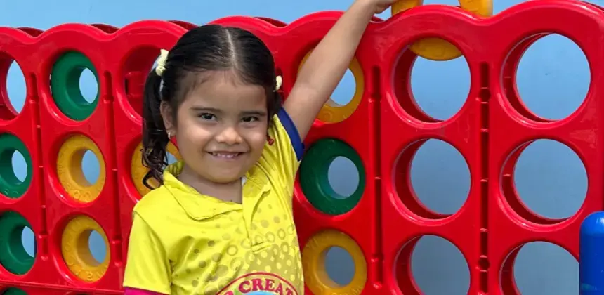 Niña sonriendo mientras juega con un tablero plástico gigante de colores.