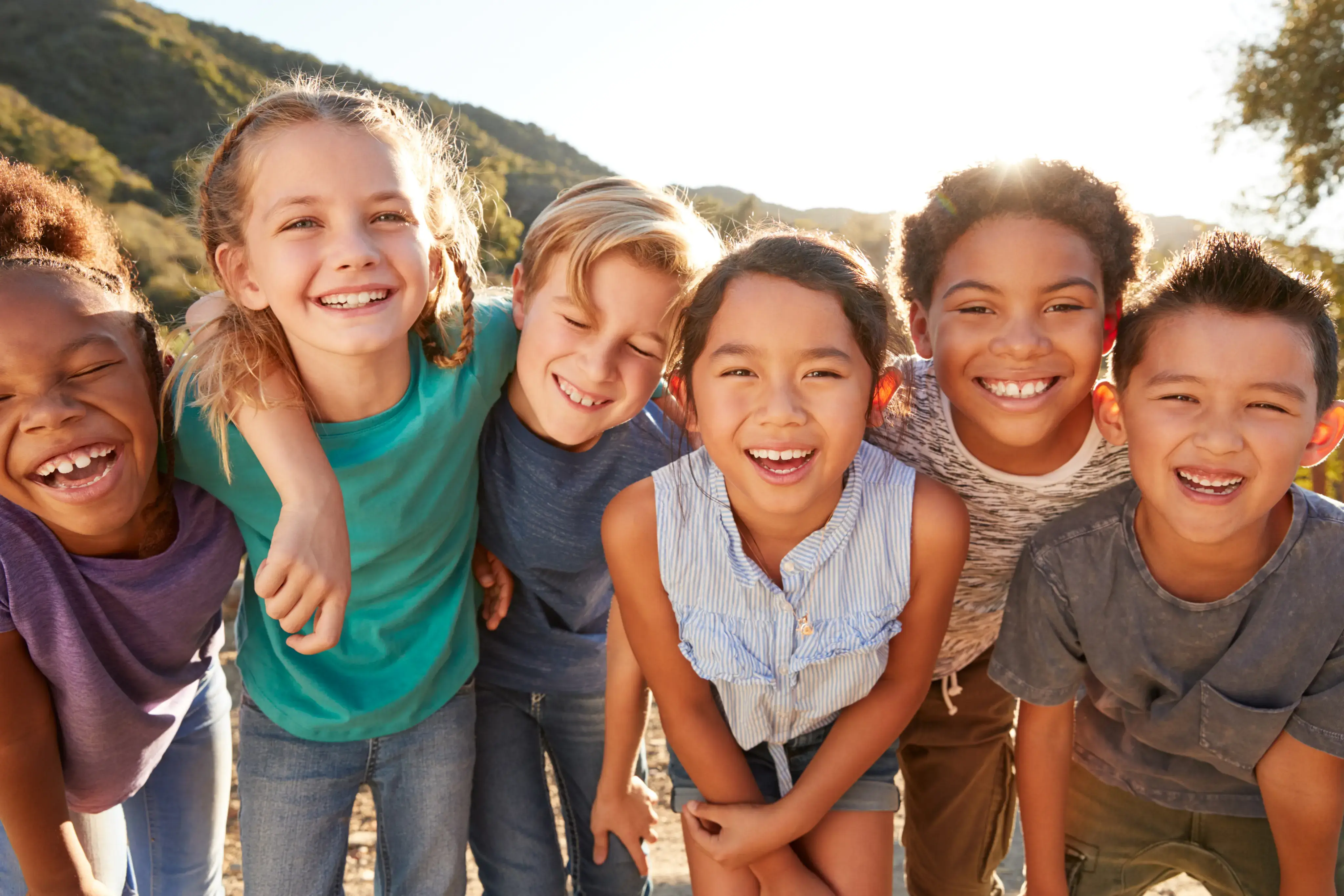 Grupo de niños abrazados y sonriendo al aire libre.