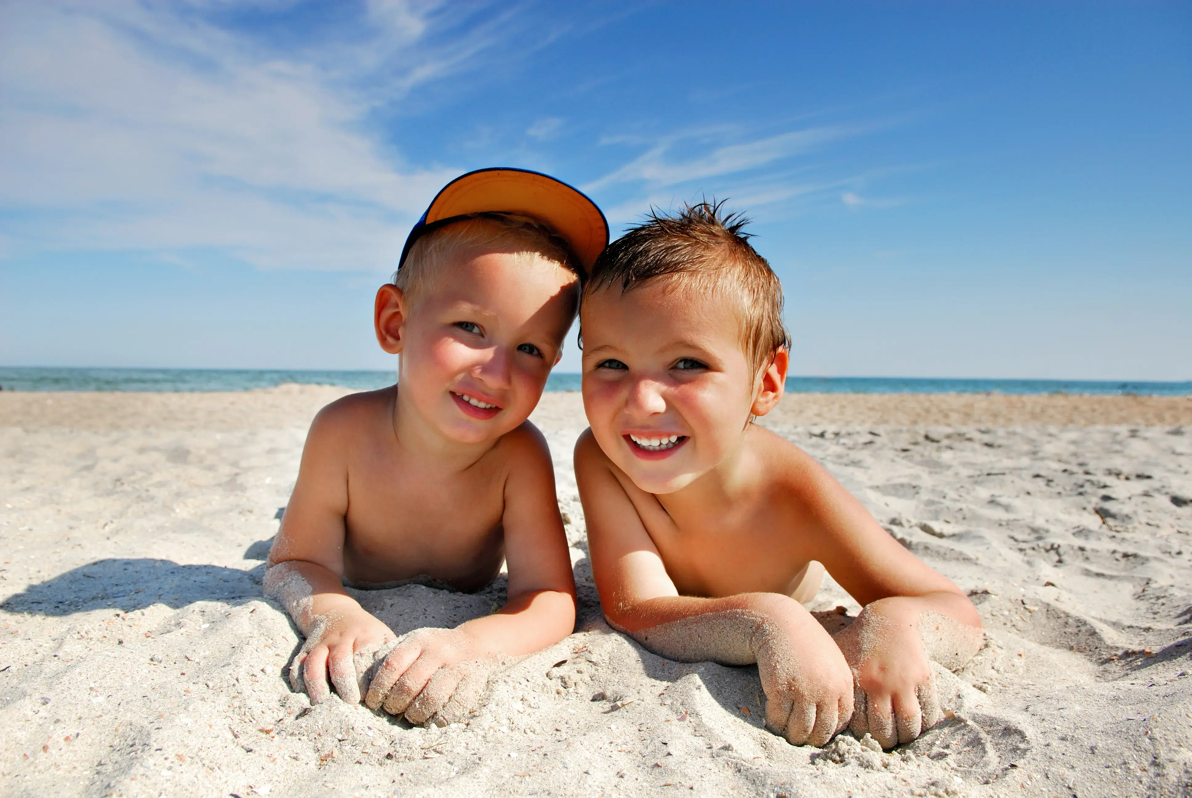 Dos niños pequeños acostados en la arena de la playa sonriendo.