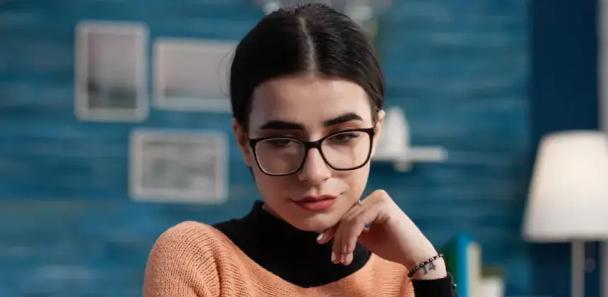 Mujer con gafas mirando hacia abajo en un ambiente interior, representando revisión o elección de lentes en Óptica Troyo.