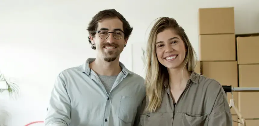 Pareja joven sonriendo en un espacio con cajas de mudanza al fondo