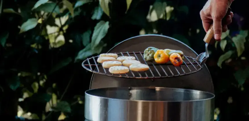 Persona asando pan y vegetales sobre una parrilla metálica en un jardín.