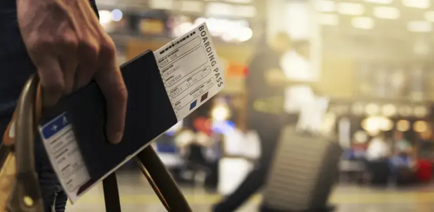 Persona sosteniendo pasaporte y pase de abordar en un aeropuerto con maletas al fondo