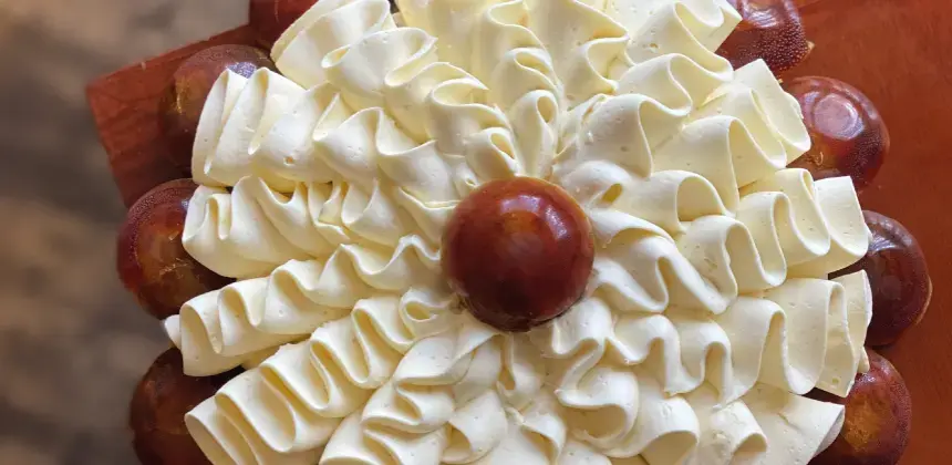 Pastel decorado con crema blanca en forma de pétalos y centro de caramelo sobre base de madera