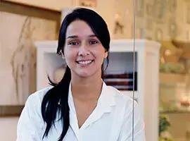 Mujer joven con bata blanca sonriendo en un entorno interior de atención o consulta.