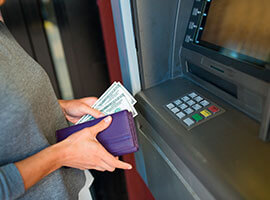 Persona retirando efectivo de un cajero automático con billetes en la mano.