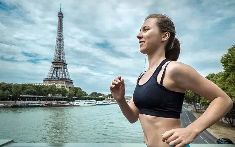 Mujer joven corriendo junto al río Sena en París, con la Torre Eiffel de fondo en un día parcialmente nublado.