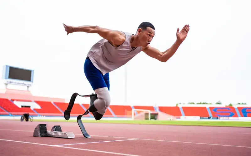 Atleta paralímpico corriendo en una pista con prótesis deportivas de carbono, en un estadio al aire libre.