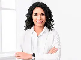 Mujer con cabello rizado y vestimenta blanca sonriendo en una oficina iluminada.
