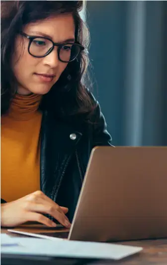 Mujer con gafas trabajando concentrada en una computadora portátil en un ambiente profesional o de estudio.