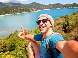 Hombre joven tomándose una selfie en la cima de una montaña con vista al mar