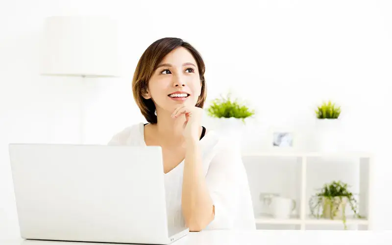 Mujer sonriente usando una computadora portátil en una oficina de estilo minimalista y decorada con plantas