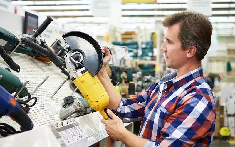 Hombre en una ferretería examinando una sierra eléctrica amarilla en la sección de herramientas