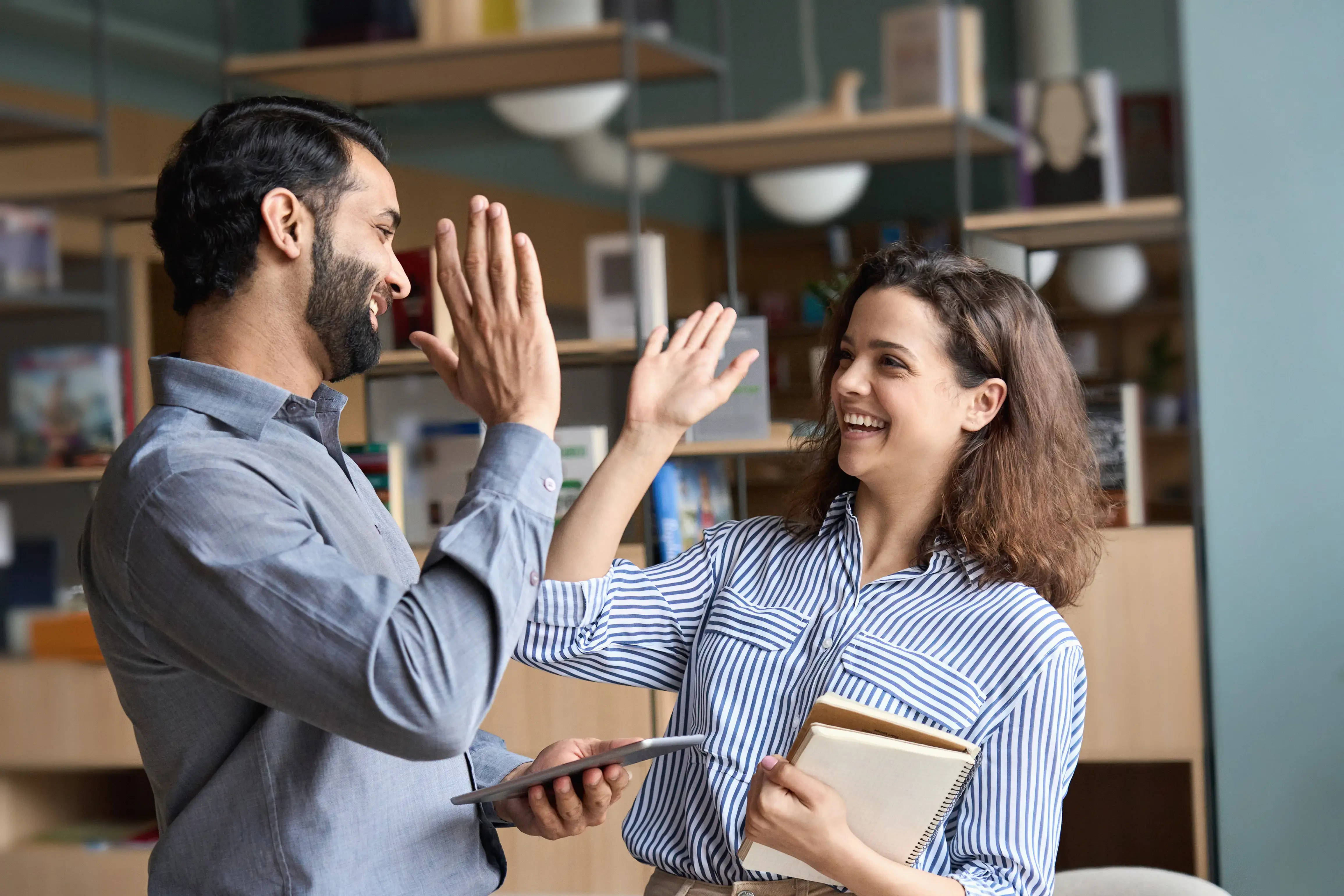 Dos compañeros de oficina sonríen y se dan un high five celebrando un logro.