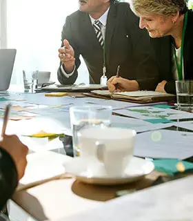 Equipo de negocios discutiendo documentos y gráficos durante una reunión, con tazas de café y papeles sobre la mesa