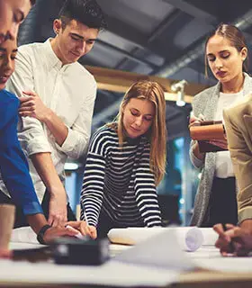 Equipo creativo de jóvenes profesionales colaborando en un proyecto alrededor de una mesa con documentos y planos