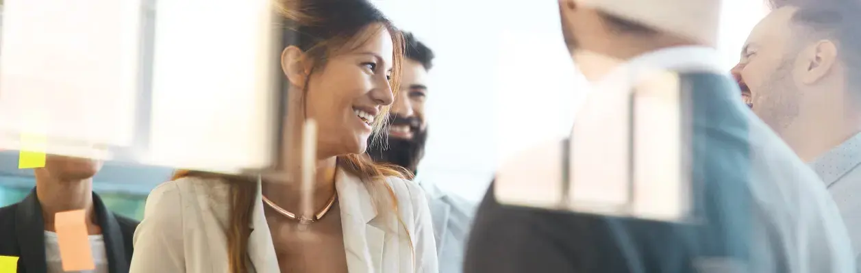 Grupo de profesionales conversando y sonriendo frente a un panel de notas adhesivas en una oficina moderna. Grupo de profesionales conversando y sonriendo frente a un panel de notas adhesivas en una oficina moderna.