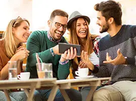 Grupo de amigos riendo mientras miran un celular en una cafetería.