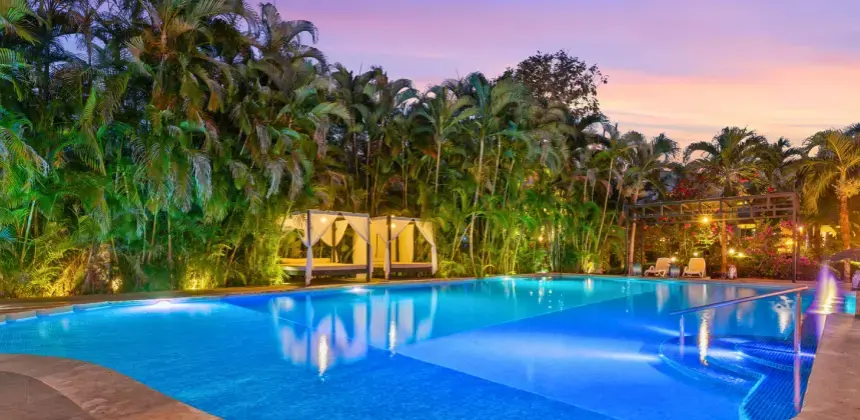 Piscina iluminada al atardecer rodeada de palmeras en hotel boutique con camas tipo balinés