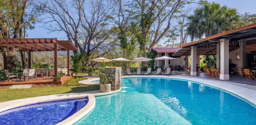 Piscina al aire libre con pérgola, sombrillas y sillas en un entorno natural del hotel