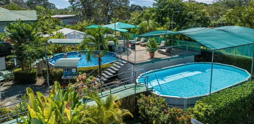 Piscinas al aire libre rodeadas de vegetación tropical en hotel con áreas de descanso