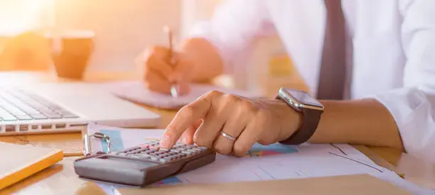 Persona usando una calculadora y tomando notas con gráficos financieros en una oficina.