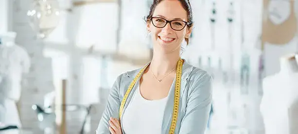 Diseñadora de modas sonriente con cinta métrica al cuello en su taller.