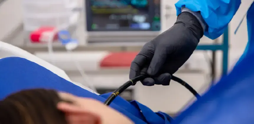 Médico realizando procedimiento endoscópico con guantes negros en paciente recostado en camilla