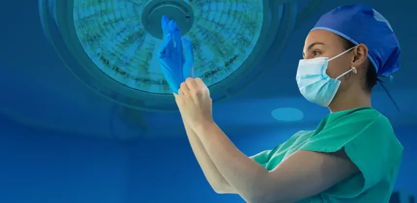 Profesional de salud colocándose guantes quirúrgicos en un quirófano iluminado.