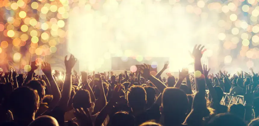 Multitud de personas levantando las manos durante un concierto iluminado con luces brillantes.