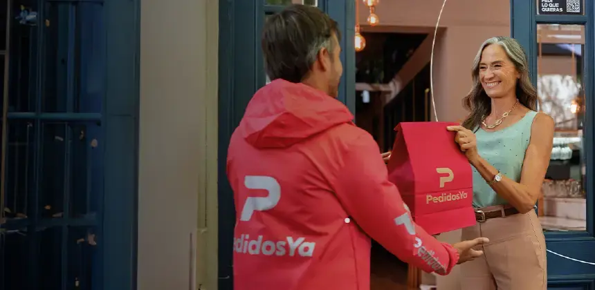 Repartidor de PedidosYa entregando un pedido a una mujer en la puerta de su casa