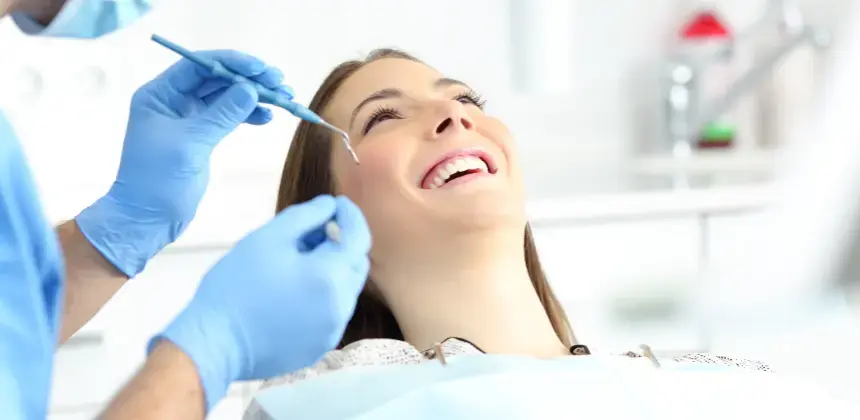 Mujer sonríe durante revisión dental mientras el odontólogo utiliza instrumentos con guantes azules