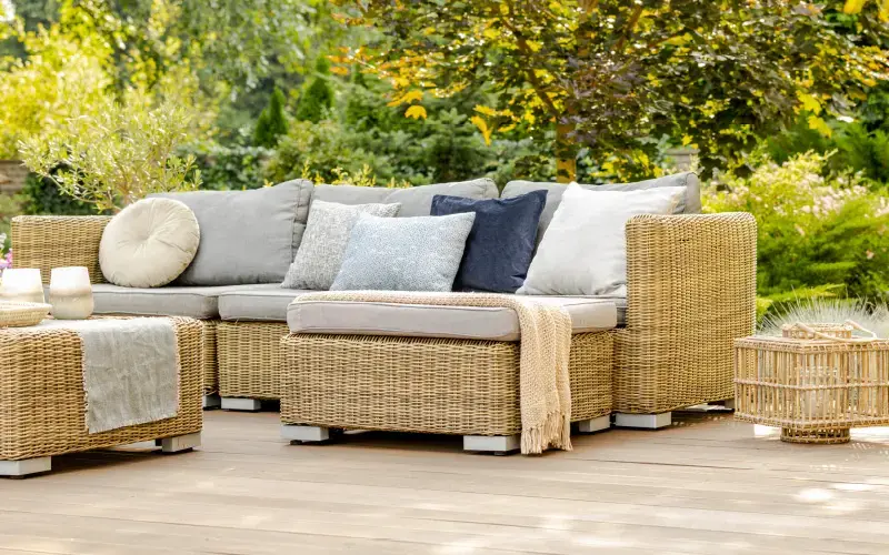 Sofá de mimbre en terraza al aire libre, decorado con cojines de distintos colores y rodeado de vegetación.