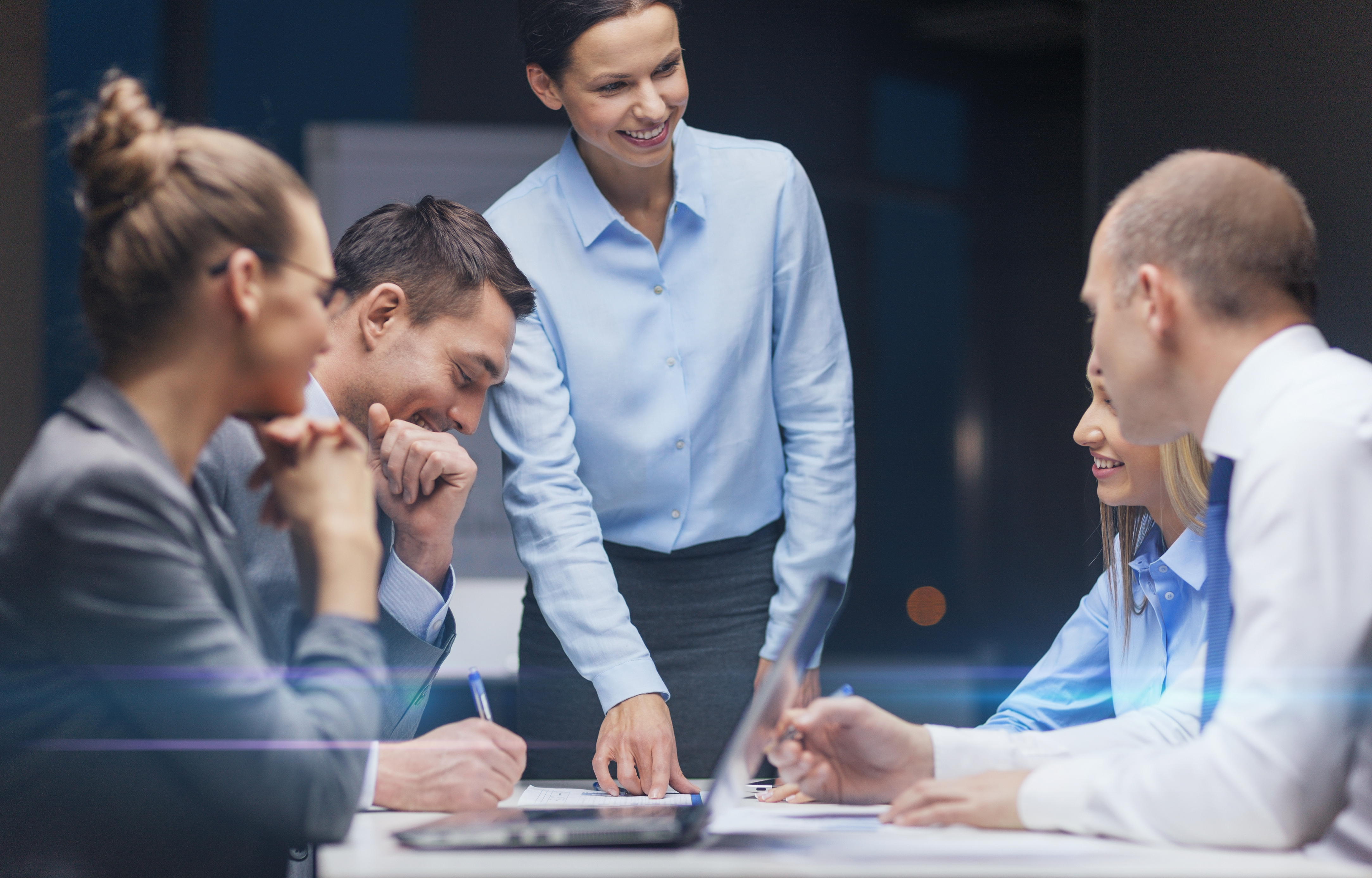 Grupo de profesionales en reunión de trabajo analizando documentos y sonriendo.
