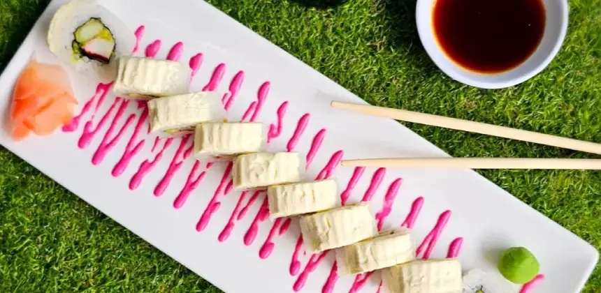 Plato de sushi con salsa rosada decorativa, acompañado de wasabi, jengibre y salsa de soya