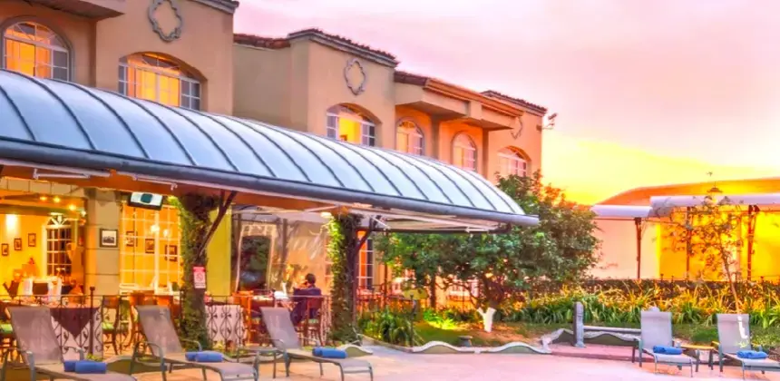 Fachada del hotel con terraza iluminada al atardecer y sillas reclinables junto a los jardines