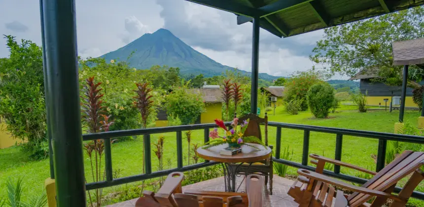 Vista desde una terraza con sillas de madera hacia el volcán Arenal rodeado de jardines verdes en el Hotel Campo Verde