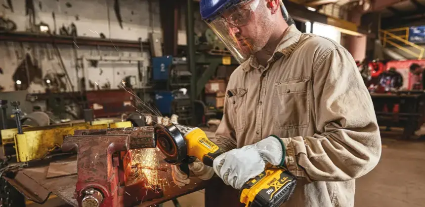 Trabajador con casco y careta protectora usando una esmeriladora en taller metálico con chispas visibles
