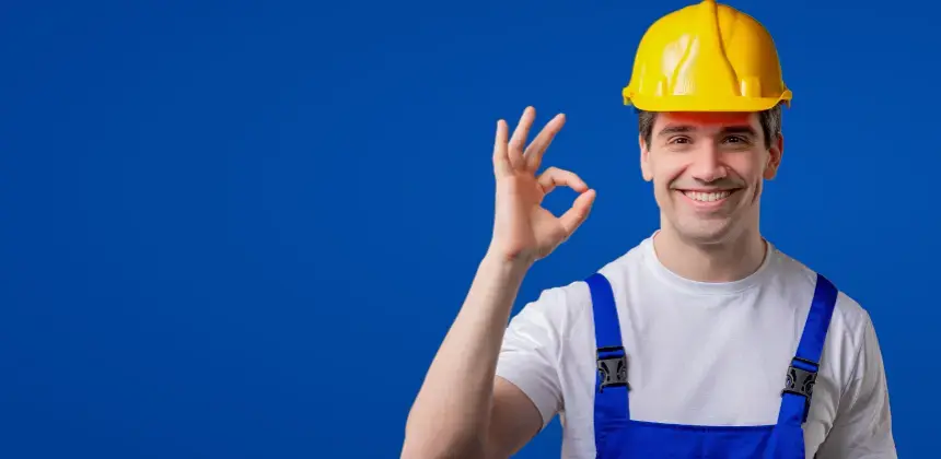 Persona con casco de seguridad amarillo haciendo un gesto de aprobación sobre fondo azul.