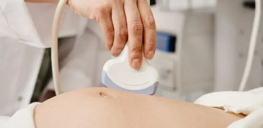 Mano de profesional realizando un ultrasonido sobre el abdomen de una persona en consulta médica