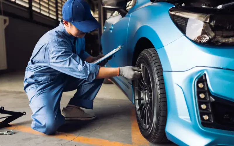 Mecánico revisando la llanta de un auto azul en un taller moderno con portapapeles en mano