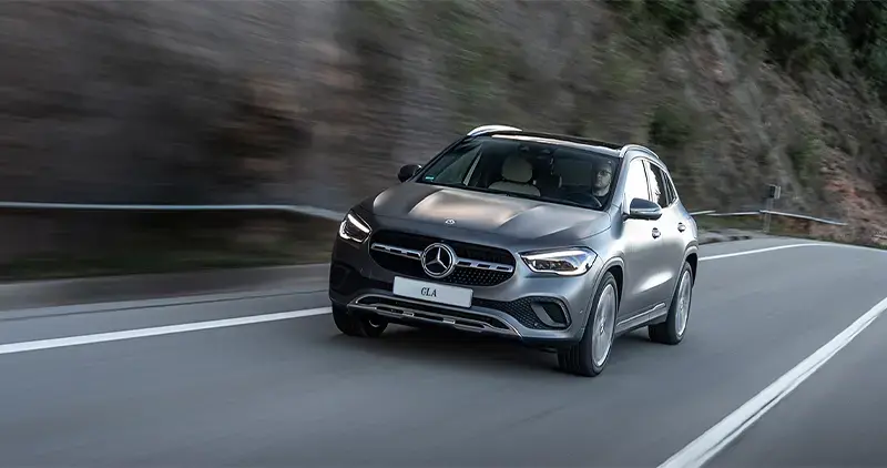Vehículo Mercedes-Benz GLA gris circulando en carretera con fondo de montaña.