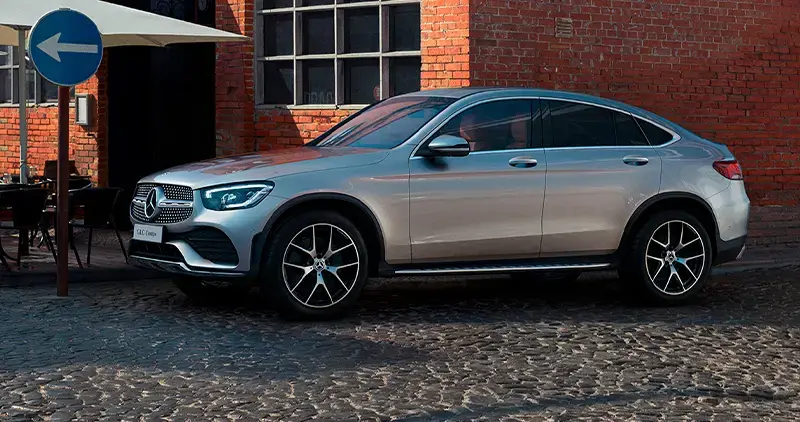Vehículo Mercedes-Benz GLC Coupé gris estacionado sobre calle empedrada frente a edificio de ladrillo.